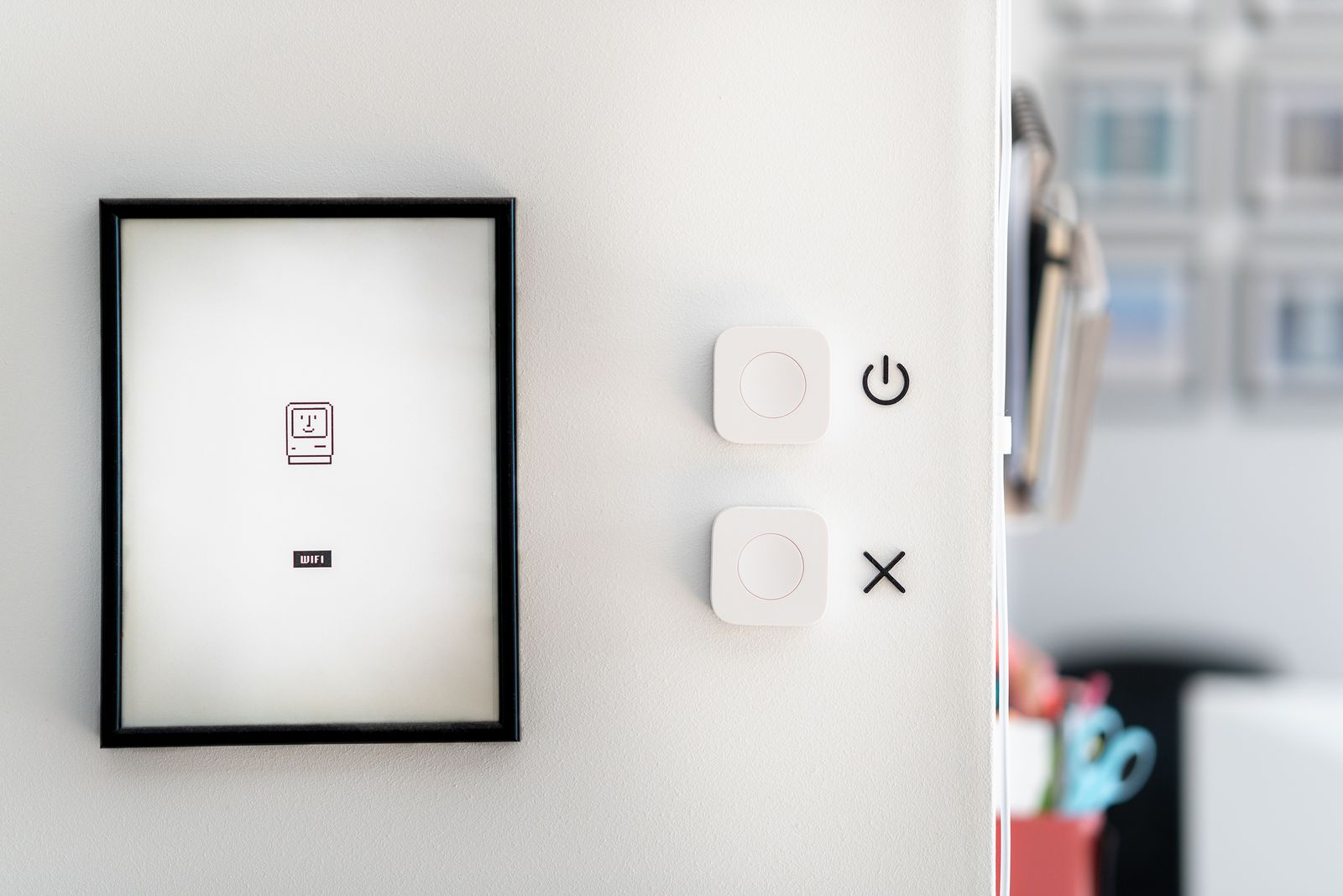 Un cadre noir accroché sur un mur blanc, avec une petite carte wifi, à côté de deux interrupteurs connectés