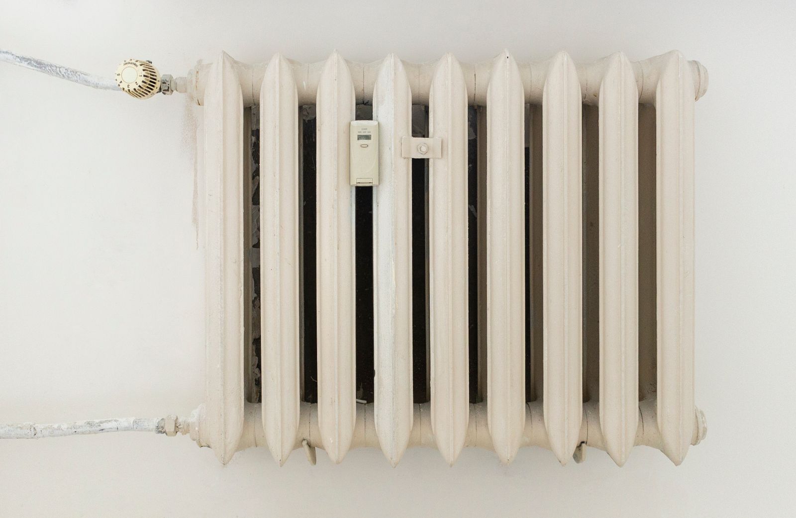 Un radiateur en fonte peint en blanc sur un mur clair, avec sa tête thermostatique graduée sur le tuyau d'arrivée