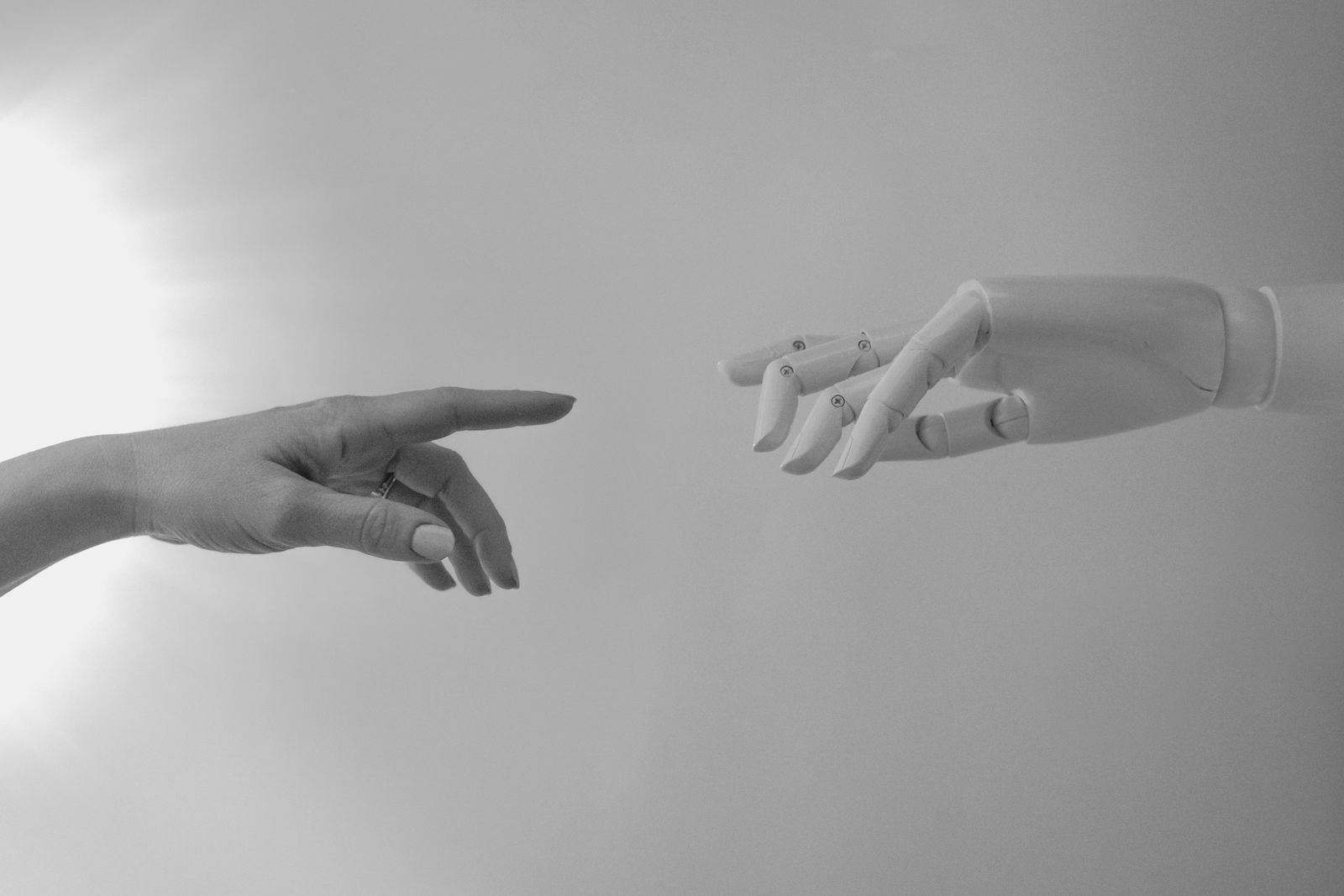 Une main humaine et une main de robot qui se tendent l'une vers l'autre, en noir et blanc