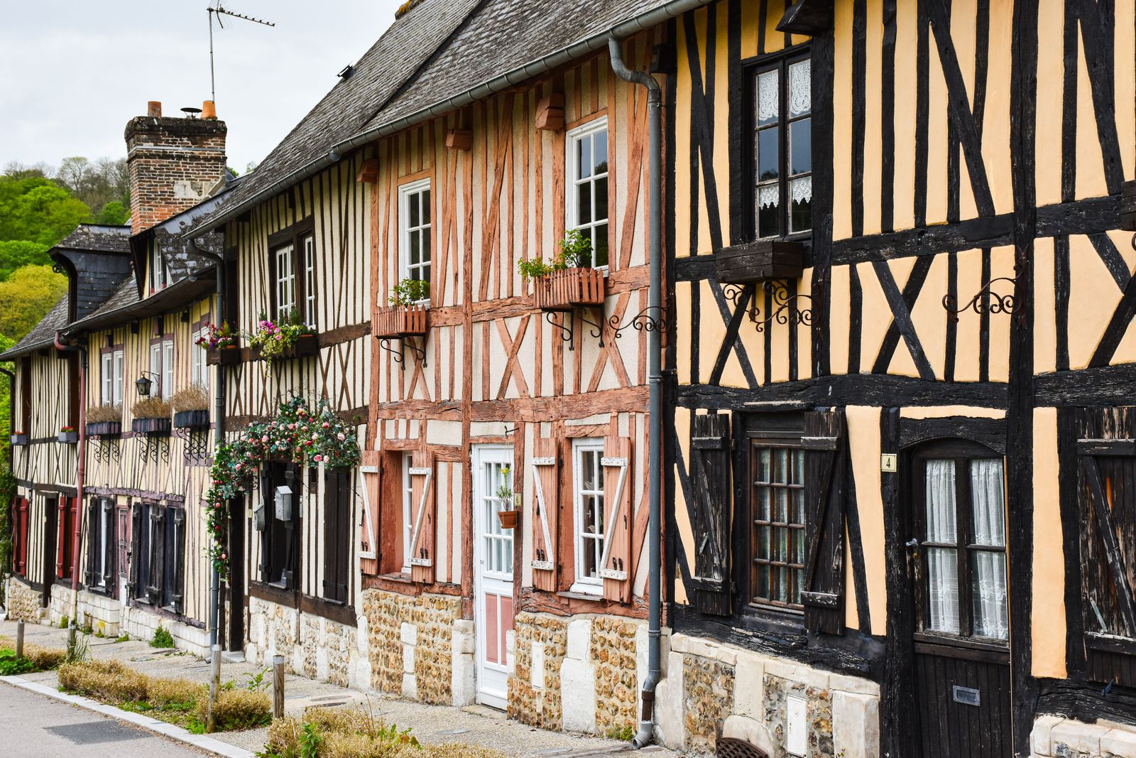 Une rangée de maisons à colombages aux volets de bois, des jardinières fleuries aux fenêtres, le long d'une rue de village