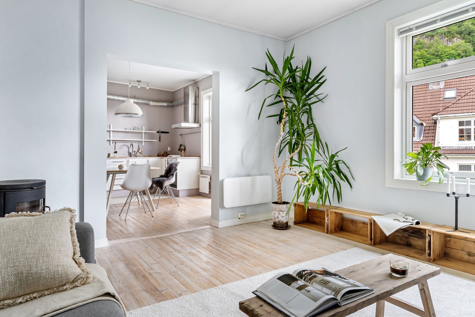 Un salon clair aux murs blancs, avec un magazine ouvert sur une table basse en bois et la cuisine en enfilade
