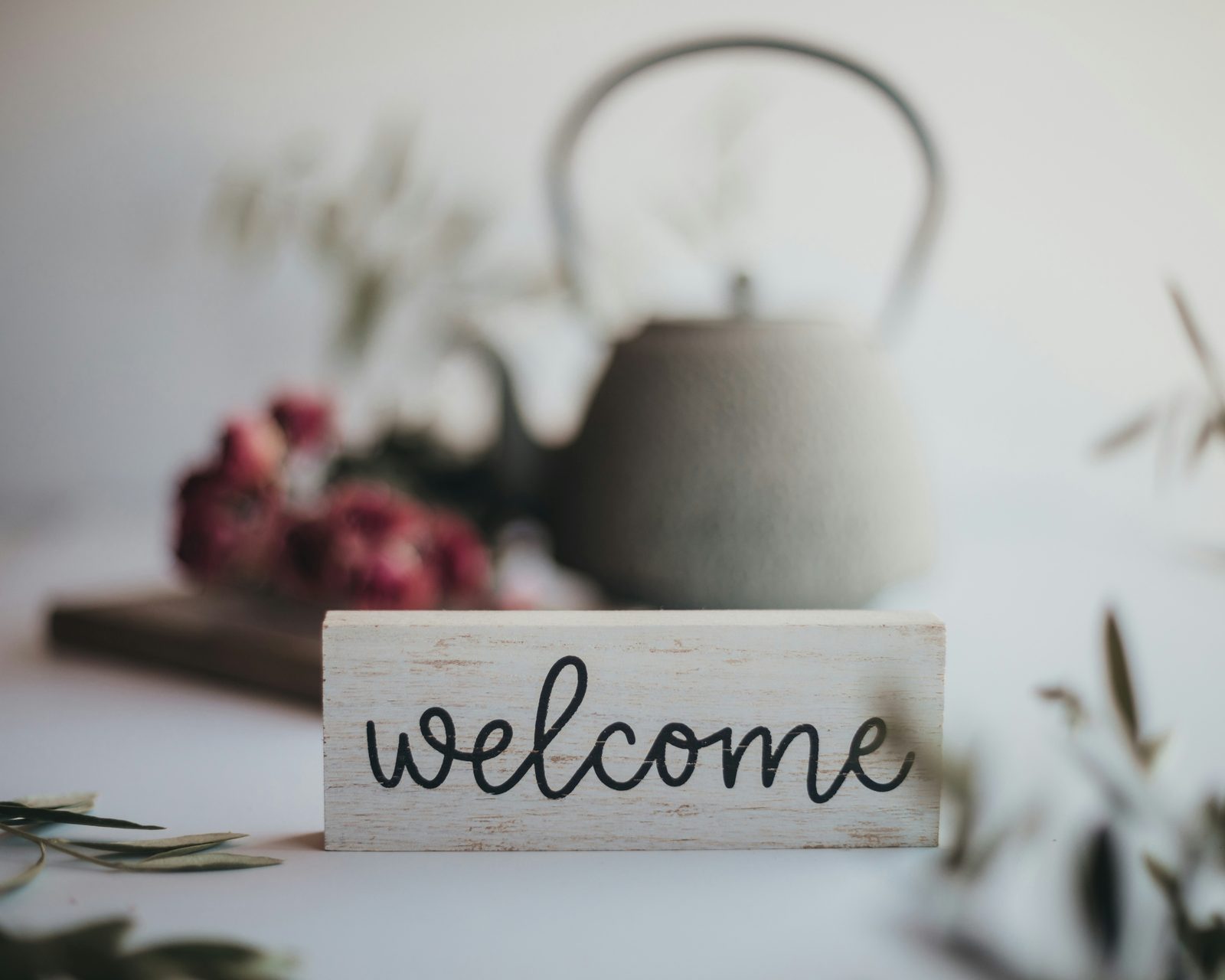 Un petit panneau de bois « welcome » posé devant une théière en fonte et des roses séchées