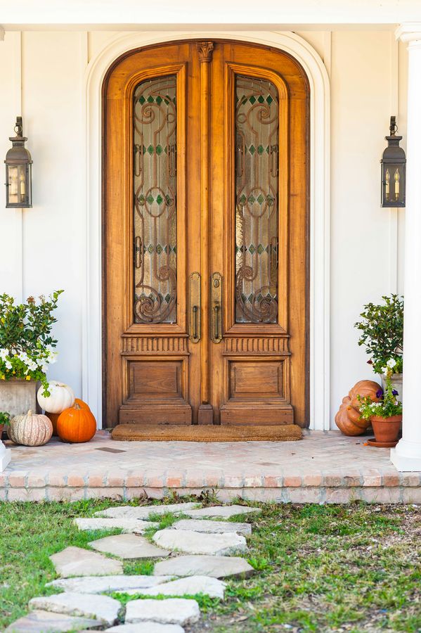 Une double porte d'entrée en bois vitré, deux lanternes de part et d'autre et des courges posées sur les marches